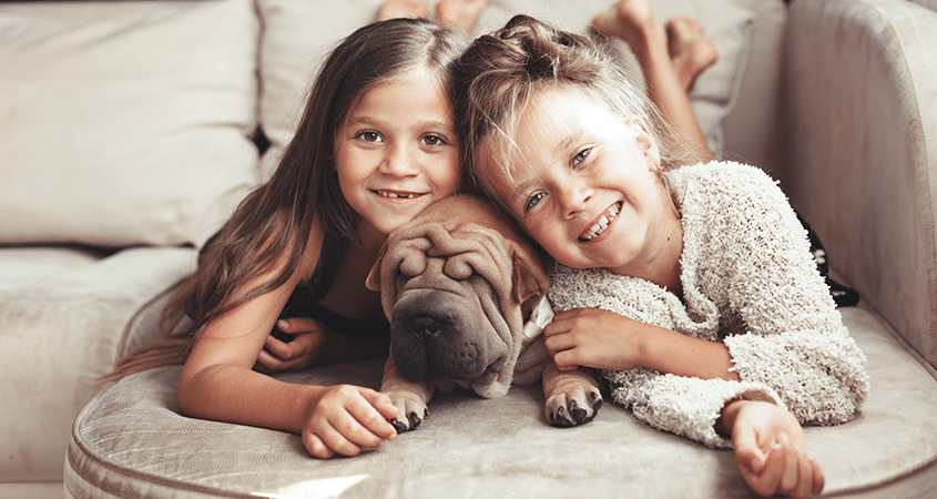 Two sisters snuggle with their pet dog.