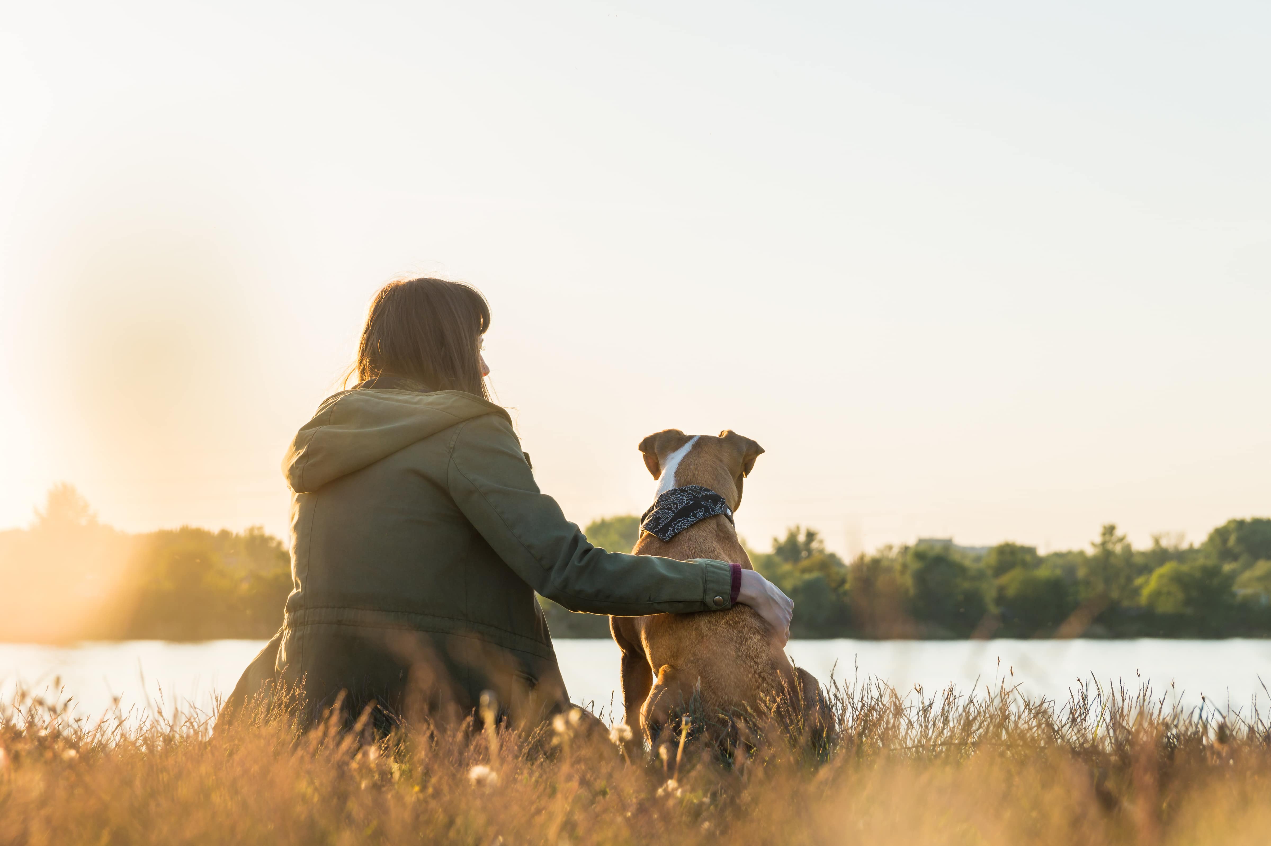 woman sits along the water with her dog