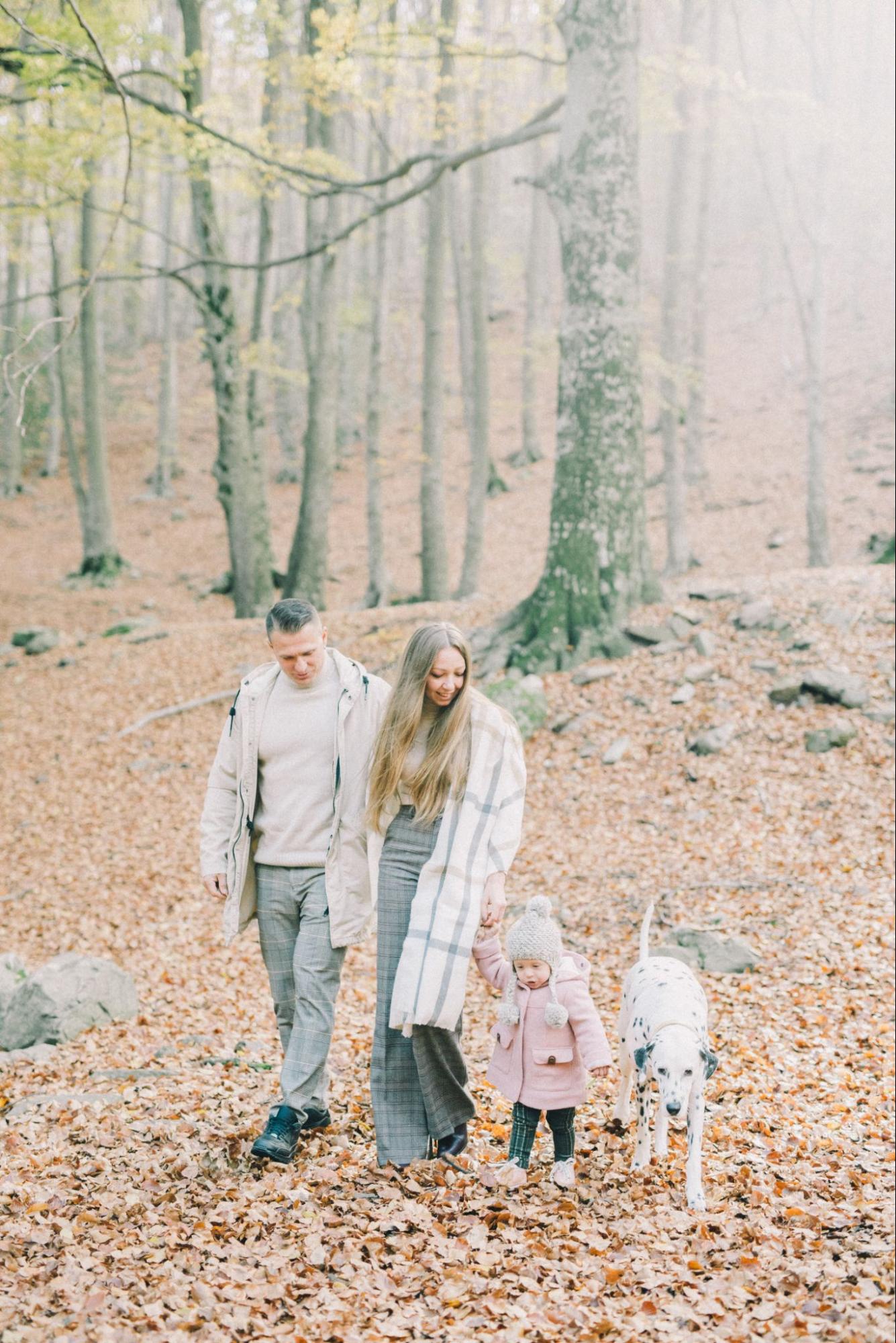 A family enjoys a walk on a beautiful fall day with their pet dalmatian.